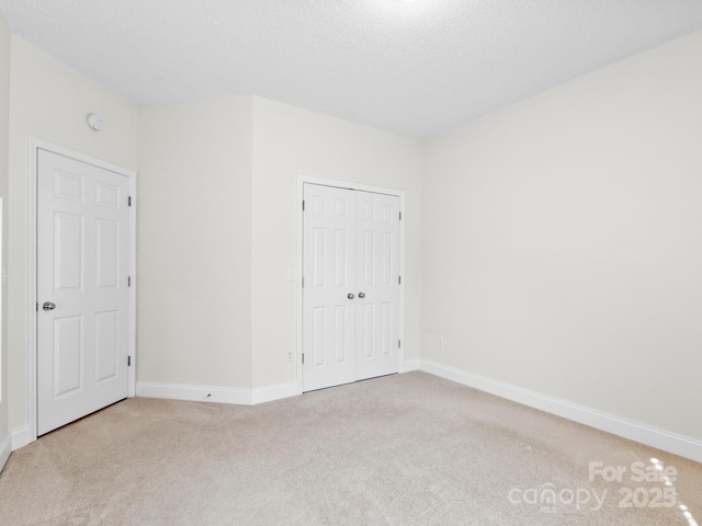 unfurnished bedroom with light carpet, baseboards, and a textured ceiling