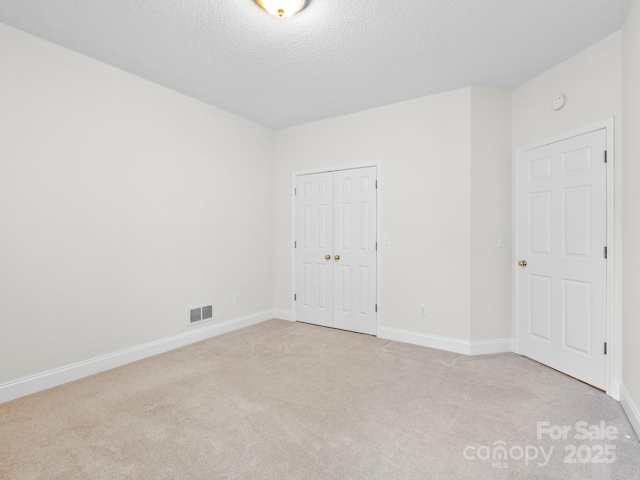 unfurnished bedroom with a textured ceiling, light colored carpet, visible vents, baseboards, and a closet