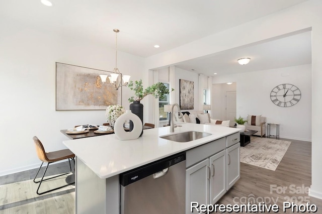 kitchen with light countertops, hanging light fixtures, stainless steel dishwasher, open floor plan, and an island with sink