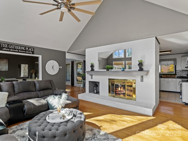 living room with light wood finished floors, ceiling fan, a fireplace, and high vaulted ceiling