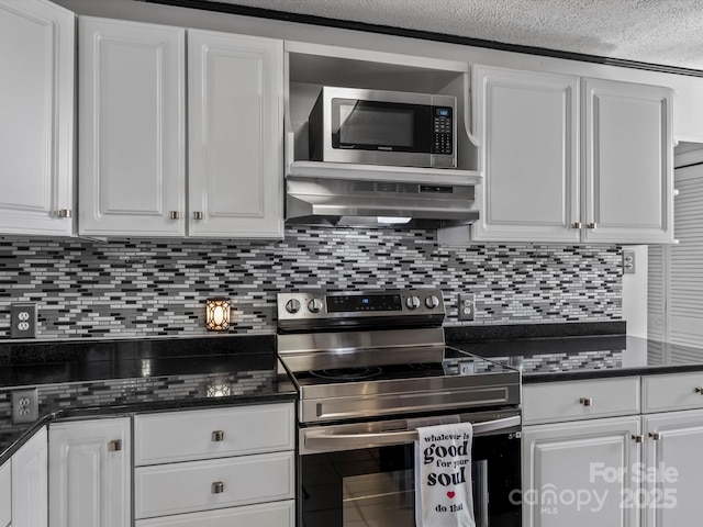 kitchen with under cabinet range hood, white cabinets, appliances with stainless steel finishes, backsplash, and dark countertops