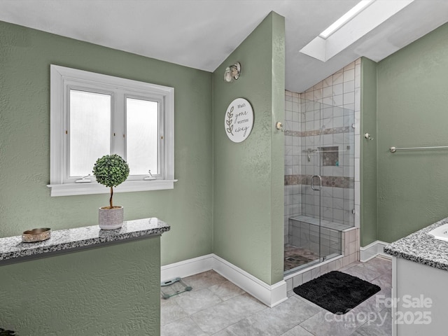 bathroom featuring a stall shower, vanity, vaulted ceiling with skylight, baseboards, and tile patterned floors