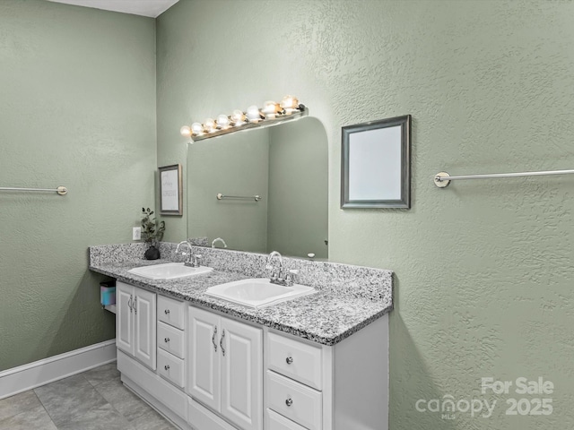 full bathroom featuring a textured wall, a sink, baseboards, and double vanity