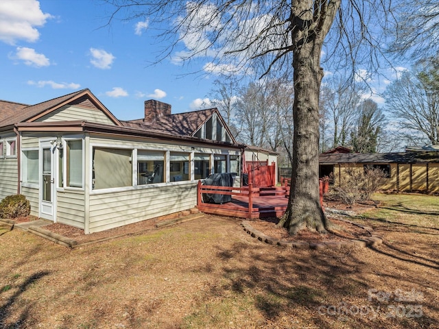 exterior space with a sunroom, a lawn, a chimney, and a wooden deck