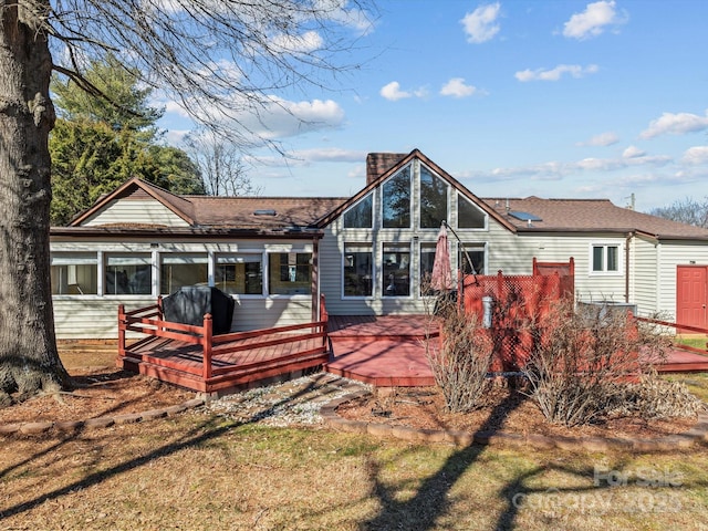 rear view of house featuring a chimney, a deck, and a lawn