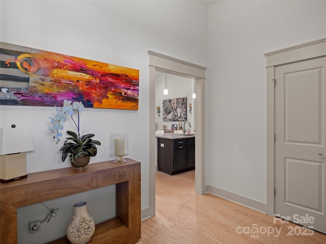 hall with baseboards, a sink, and light wood-style floors