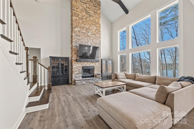 living area with baseboards, stairway, beamed ceiling, wood finished floors, and a stone fireplace