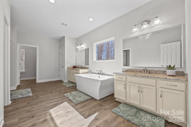 bathroom featuring wood finished floors, two vanities, a sink, a freestanding bath, and visible vents