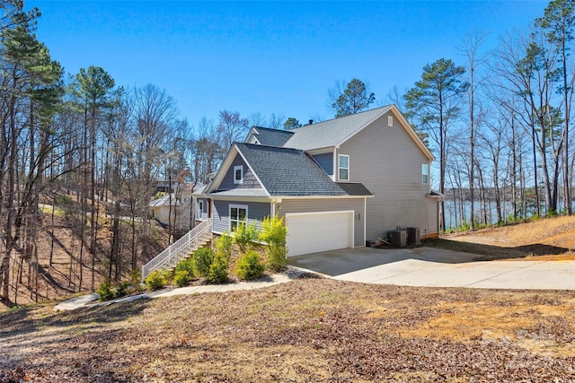 view of side of property featuring a shingled roof, concrete driveway, stairway, central AC unit, and a garage