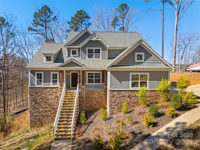 craftsman-style house featuring stone siding, a shingled roof, stairs, and covered porch