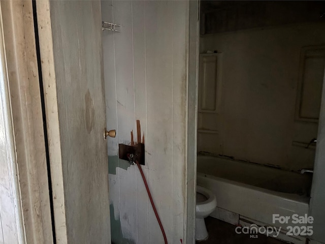 bathroom featuring toilet, wooden walls, and a bathtub