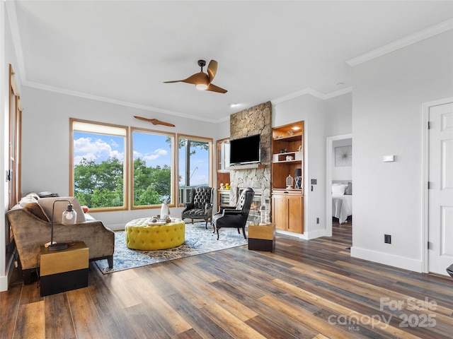 living area featuring dark wood-style floors, baseboards, a stone fireplace, and ornamental molding