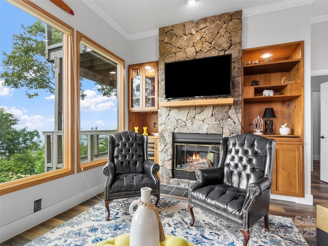 living area featuring built in features, baseboards, ornamental molding, wood finished floors, and a stone fireplace