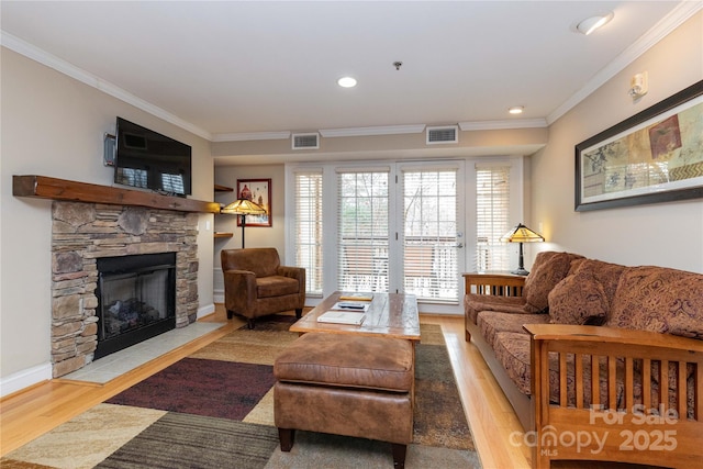 living area featuring ornamental molding, visible vents, a stone fireplace, and wood finished floors