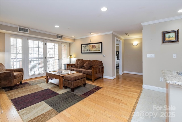 living room featuring ornamental molding, light wood-style flooring, visible vents, and baseboards