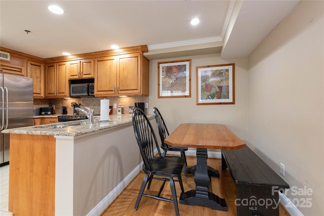 kitchen featuring stainless steel appliances, a peninsula, a sink, brown cabinets, and tasteful backsplash