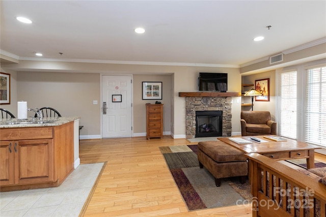 living area featuring a stone fireplace, visible vents, baseboards, ornamental molding, and light wood-type flooring