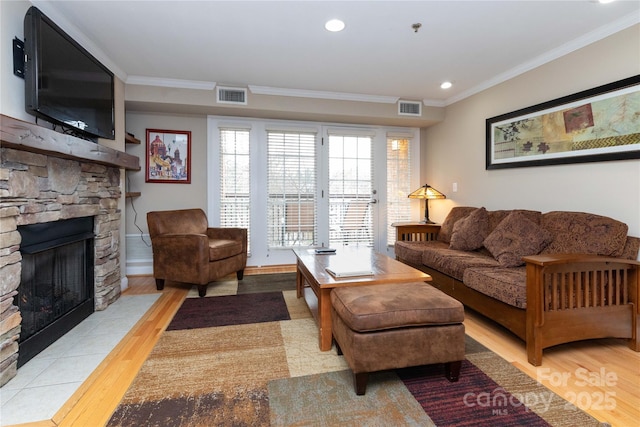 living area with visible vents, crown molding, and a stone fireplace