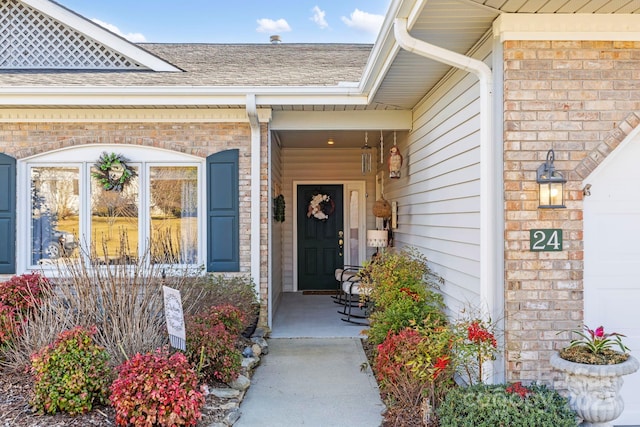 view of exterior entry featuring brick siding, covered porch, an attached garage, and roof with shingles