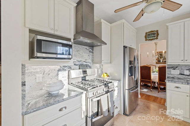 kitchen with light stone countertops, decorative backsplash, appliances with stainless steel finishes, white cabinetry, and wall chimney range hood