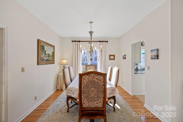 dining space featuring baseboards, light wood-type flooring, and a chandelier