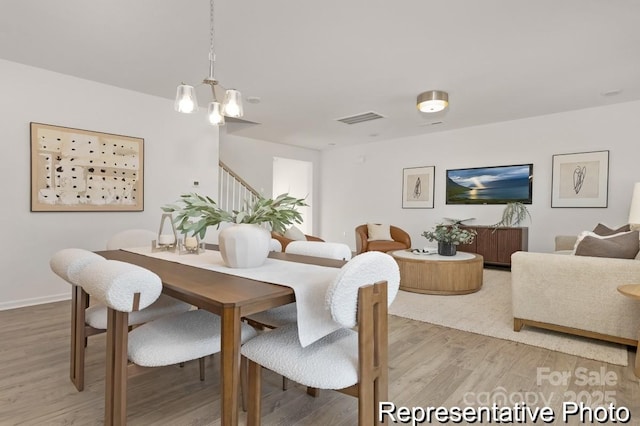 dining space featuring a notable chandelier, light wood finished floors, visible vents, baseboards, and stairs