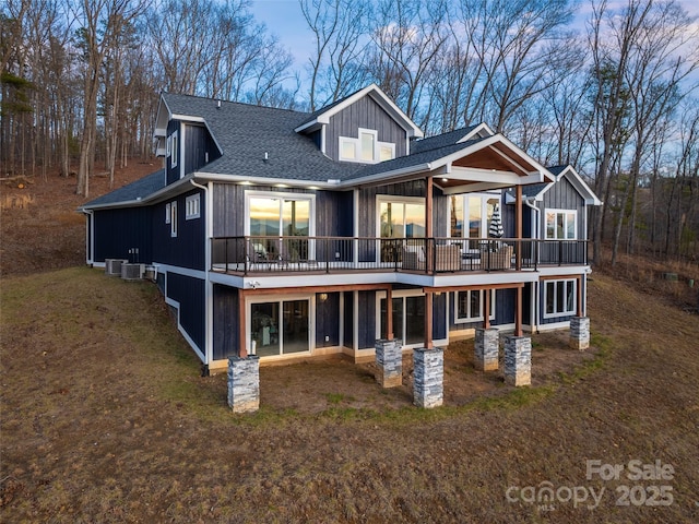 rear view of house with a shingled roof, central AC unit, a wooden deck, and a yard