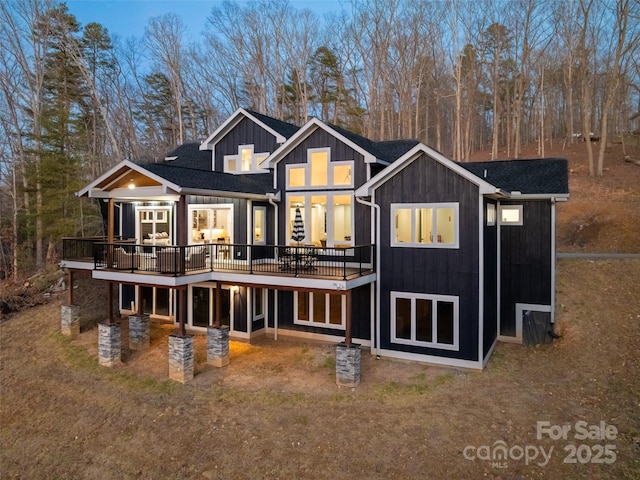 rear view of house with board and batten siding, roof with shingles, and a deck