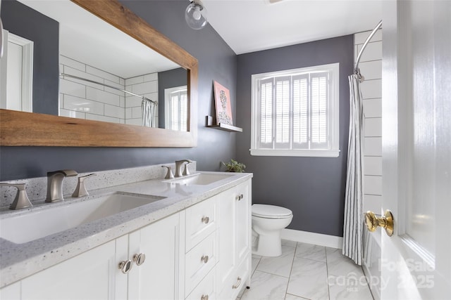 bathroom featuring double vanity, marble finish floor, baseboards, and a sink