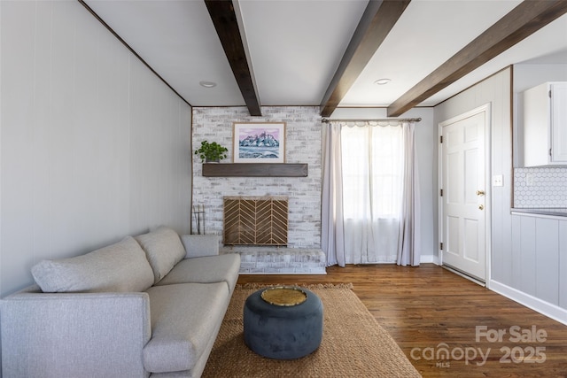 living area featuring a brick fireplace, beamed ceiling, and wood finished floors