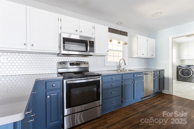 kitchen featuring stainless steel appliances, a sink, white cabinets, blue cabinetry, and washer / clothes dryer