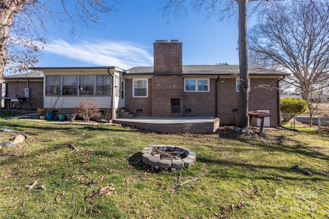 rear view of property with a lawn, an outdoor fire pit, crawl space, and a sunroom