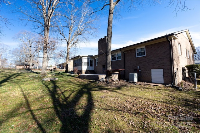 back of property featuring central air condition unit, brick siding, fence, a yard, and a chimney