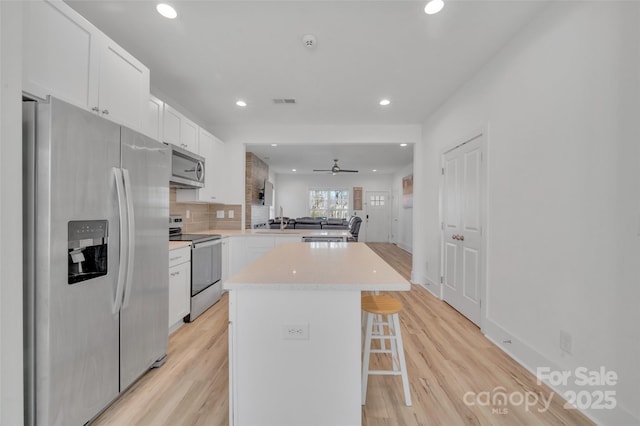 kitchen featuring a peninsula, white cabinetry, appliances with stainless steel finishes, light wood-type flooring, and a kitchen bar