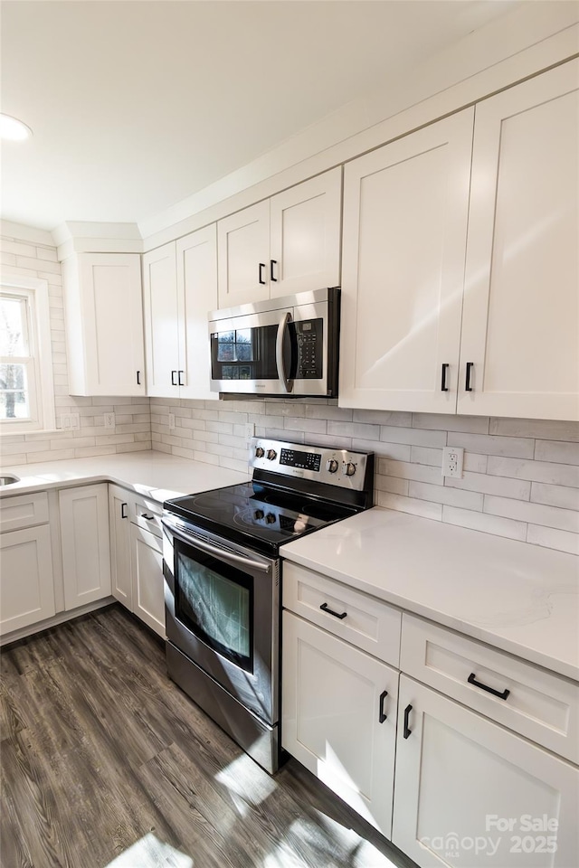 kitchen featuring dark wood-style floors, stainless steel appliances, light countertops, white cabinetry, and backsplash