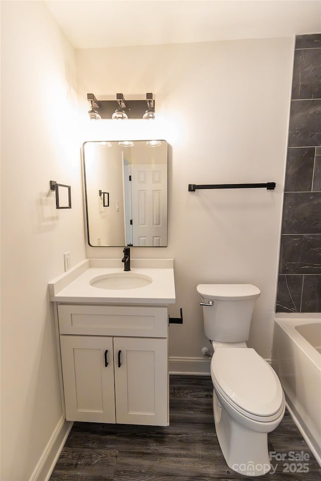 bathroom featuring toilet, baseboards, wood finished floors, and vanity