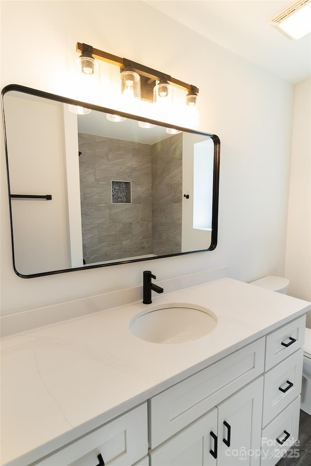 bathroom featuring toilet, visible vents, a tile shower, and vanity