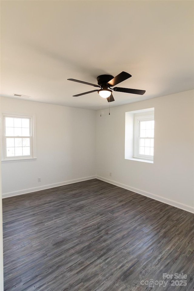 spare room with dark wood-style floors, visible vents, baseboards, and a ceiling fan