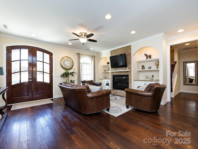 living area with built in shelves, a fireplace, ornamental molding, french doors, and dark wood finished floors