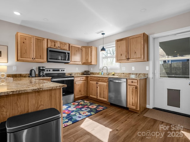 kitchen with pendant lighting, stainless steel appliances, light wood-style flooring, a sink, and light stone countertops