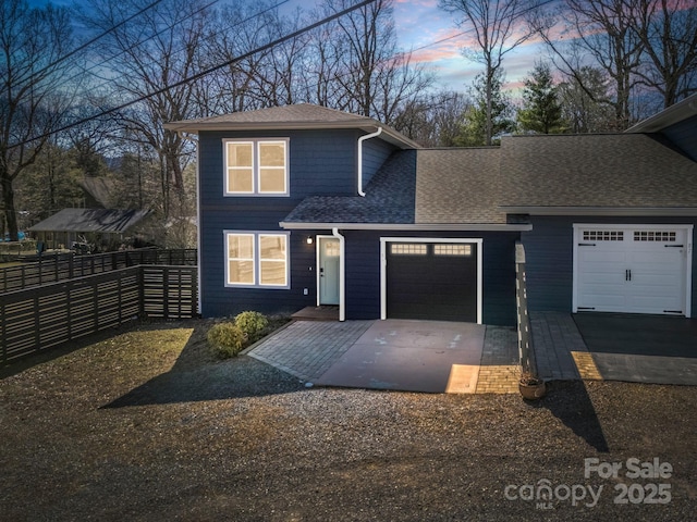 traditional home featuring driveway, a shingled roof, an attached garage, and fence