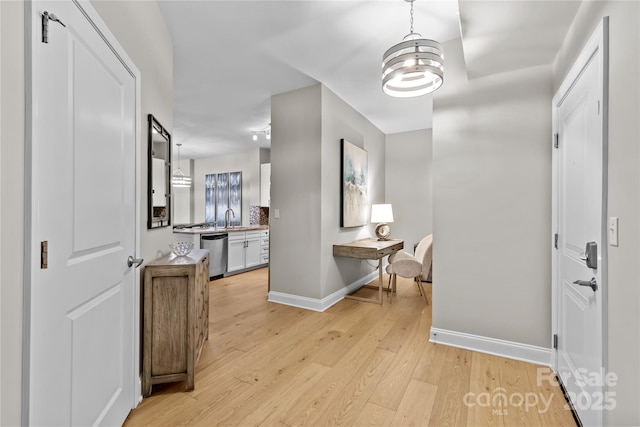 hallway with light wood-type flooring, baseboards, and a sink