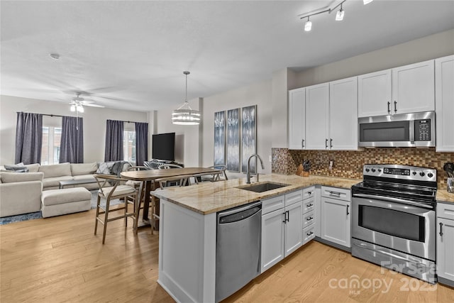 kitchen with appliances with stainless steel finishes, white cabinets, a sink, and open floor plan