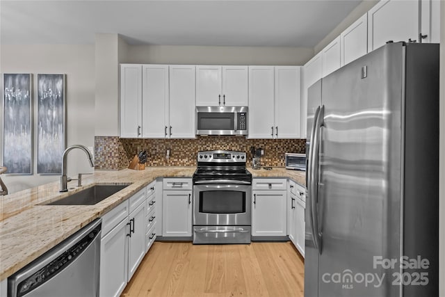 kitchen with stainless steel appliances, light wood-style floors, white cabinetry, a sink, and light stone countertops