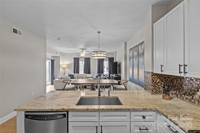 kitchen with backsplash, stainless steel dishwasher, open floor plan, white cabinetry, and a sink