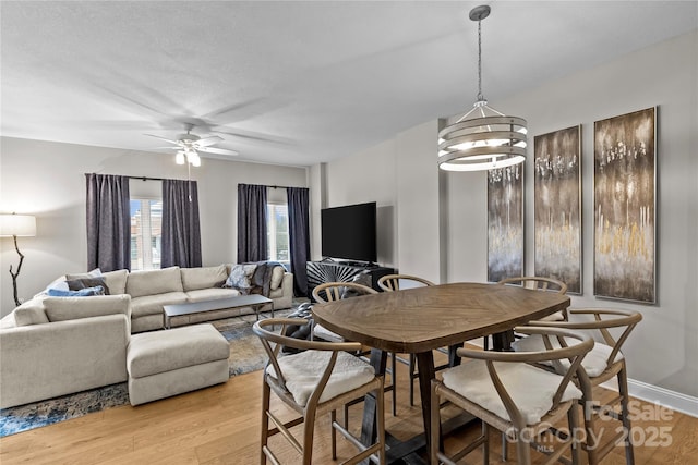 dining space featuring light wood-type flooring, baseboards, and ceiling fan with notable chandelier