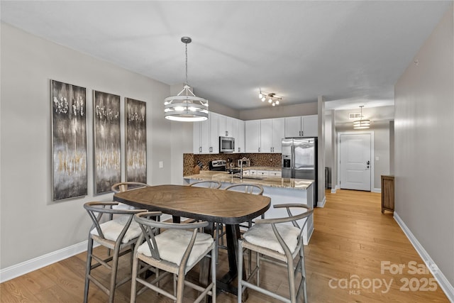 dining space with light wood-type flooring, visible vents, and baseboards