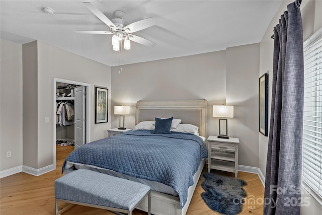 bedroom featuring ceiling fan, light wood-style flooring, baseboards, and a walk in closet