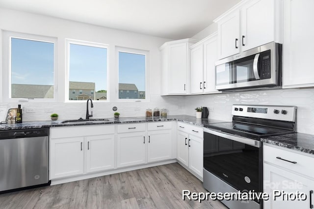 kitchen featuring stainless steel appliances, tasteful backsplash, white cabinetry, a sink, and dark stone counters