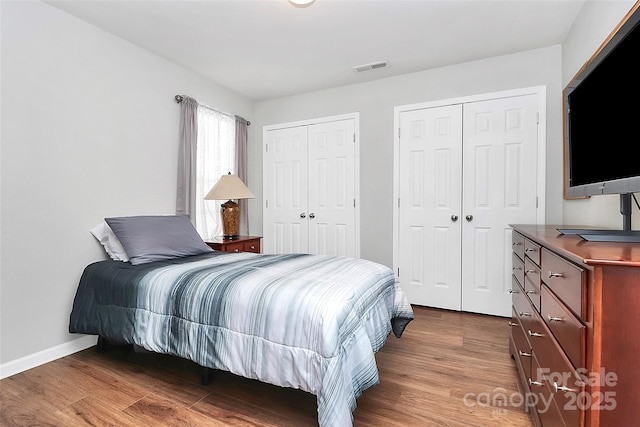 bedroom with baseboards, visible vents, two closets, and wood finished floors